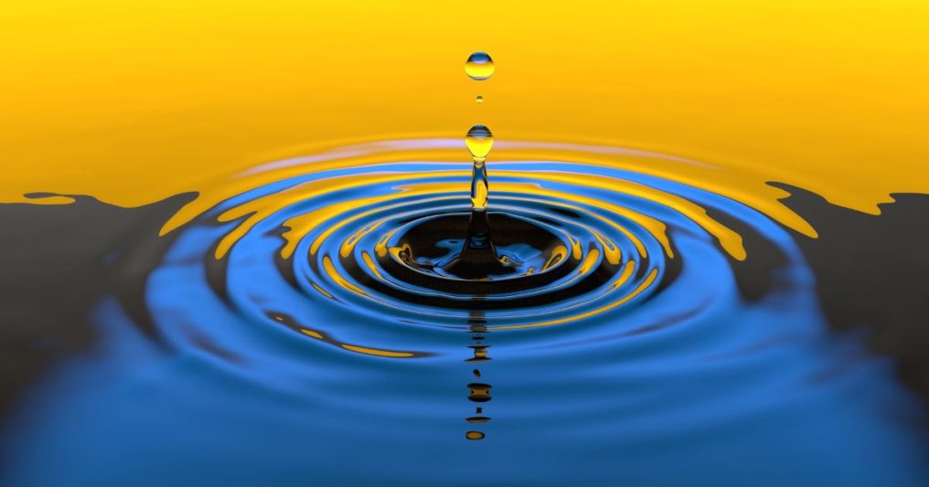 A close-up of water droplets creating ripples in a pool, with a yellow and blue gradient sky—symbolizing the ripple effect of federal tax law changes on real estate.
