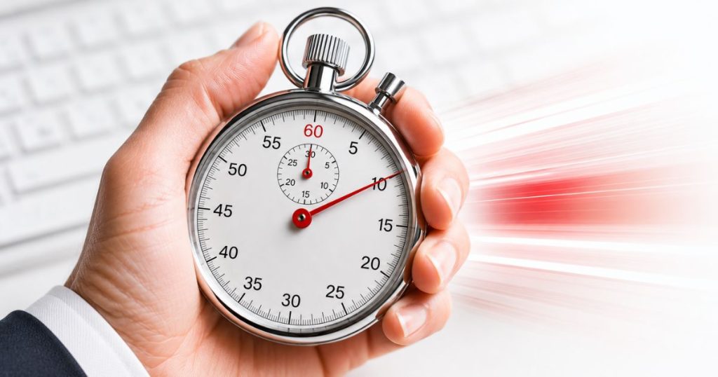 Close-up image of a hand holding a large silver stopwatch against a bright white background with a softly blurred keyboard. Red motion streaks behind the stopwatch create a sense of urgency and speed, symbolizing the time-sensitive nature of cyber insurance reporting after wire fraud incidents.